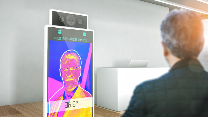 Man standing in front of temperature scanning kiosk in office building.